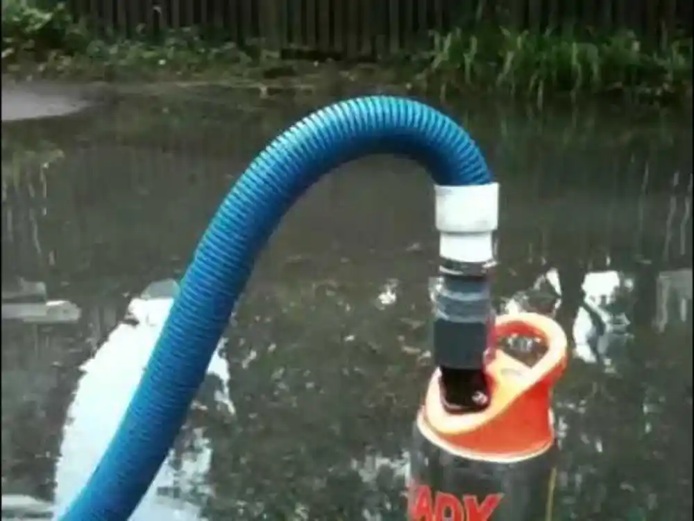Technician in waders/boots extracting floodwater with a submersible pump or wet-vac in a — Flood Damage Cleanup in Fairfax, VA